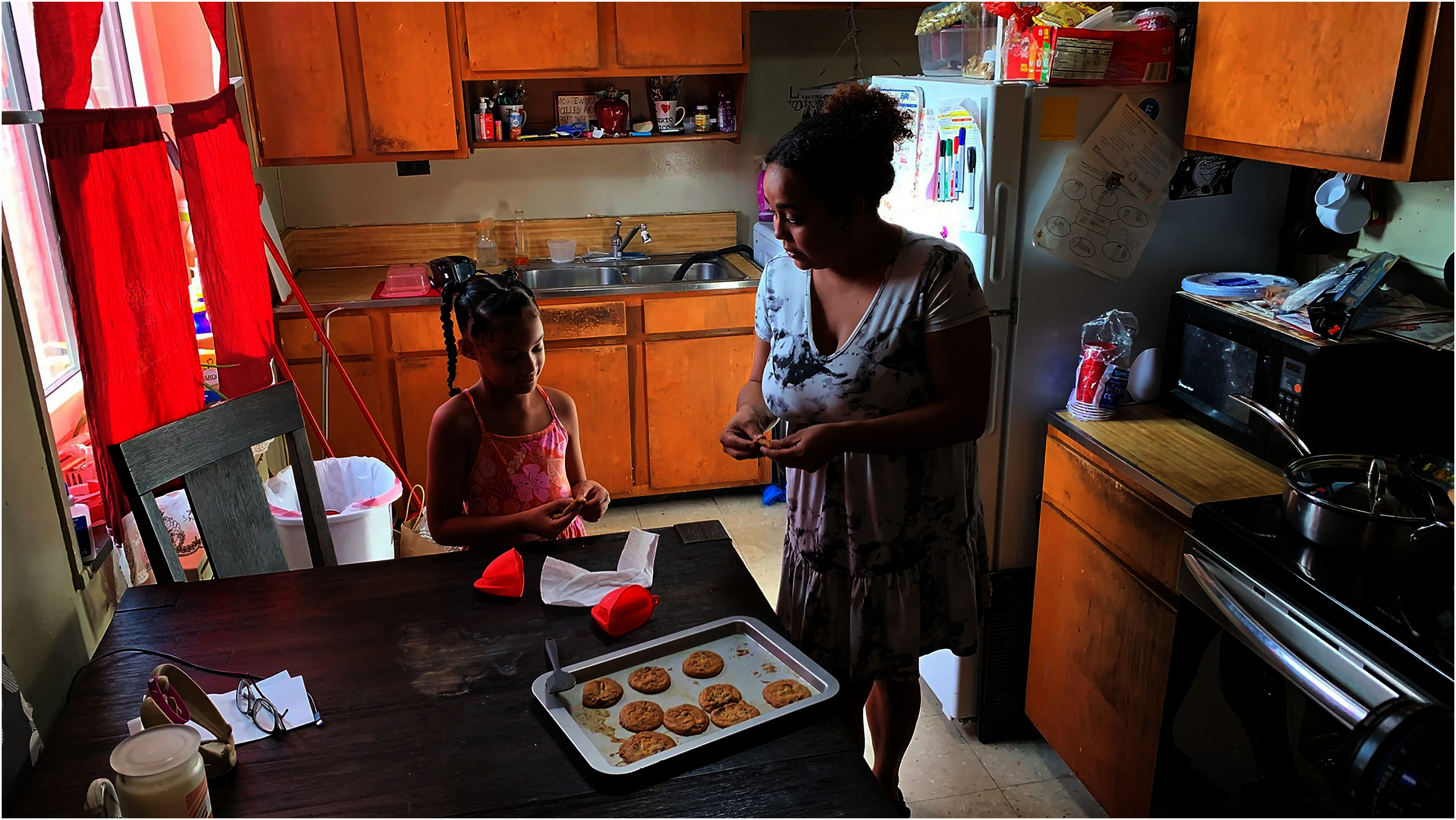 A woman and her daughter stand in a small kitchen making cookies