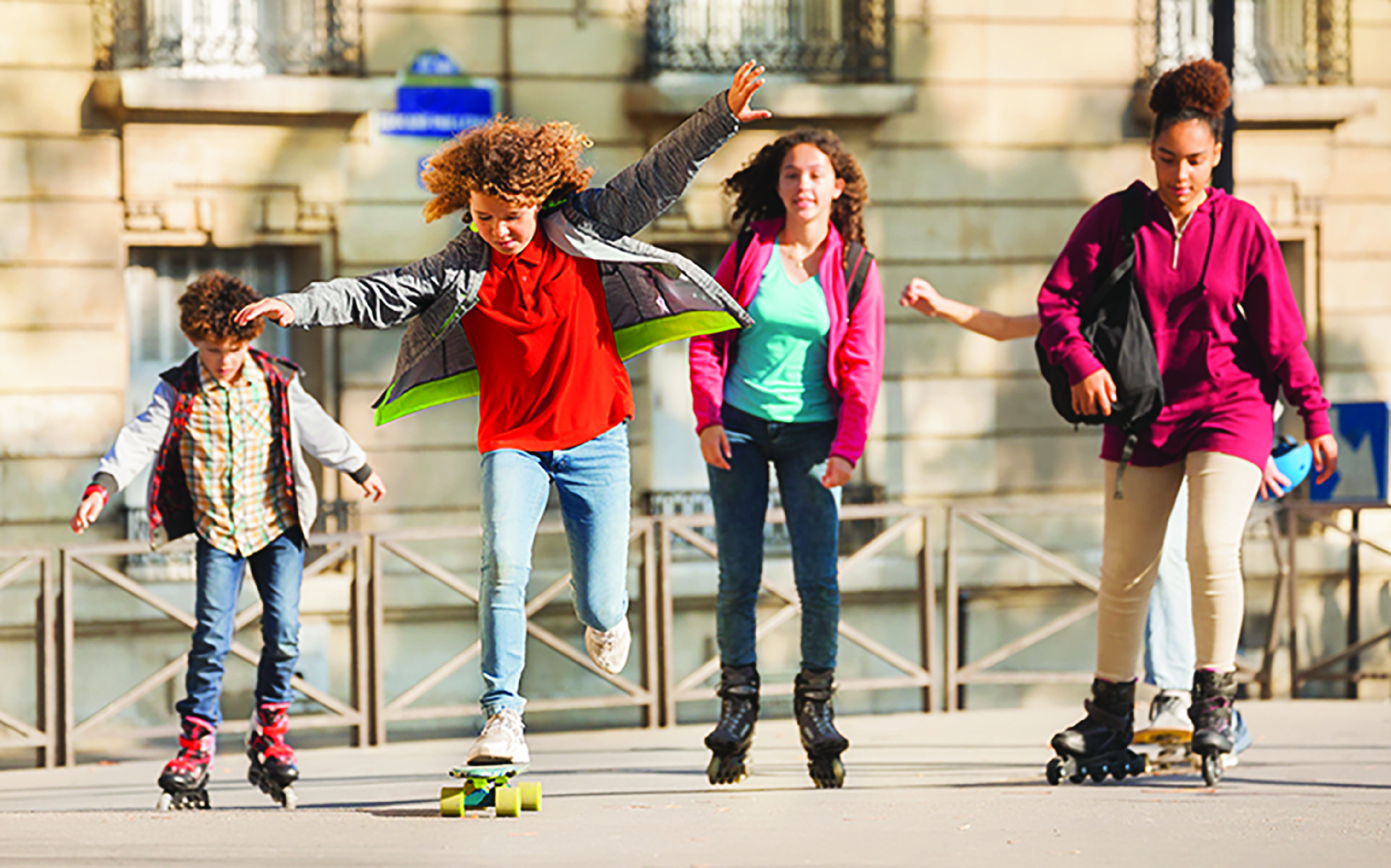 Four children playing on rollerblades and a skateboard