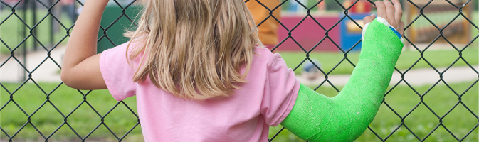 Photograph of a girl with a cast on her arm looking into a playground