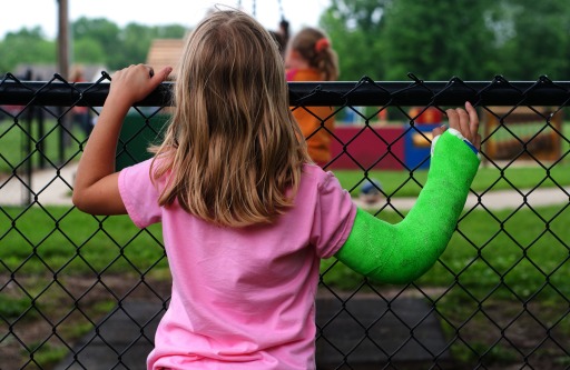 Photograph of a girl with a cast on her arm looking into a playground