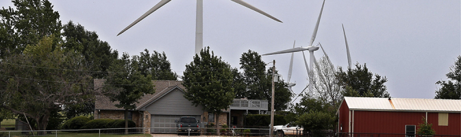 House and barn with large windmills rising behind them