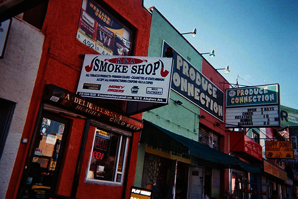 Street scene showing a smoke shop next door to a store selling produce.