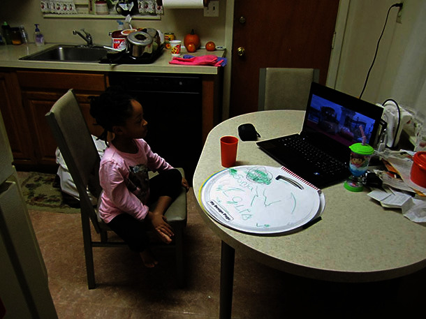 Child sitting at a kitchen table watching a movie on a computer.