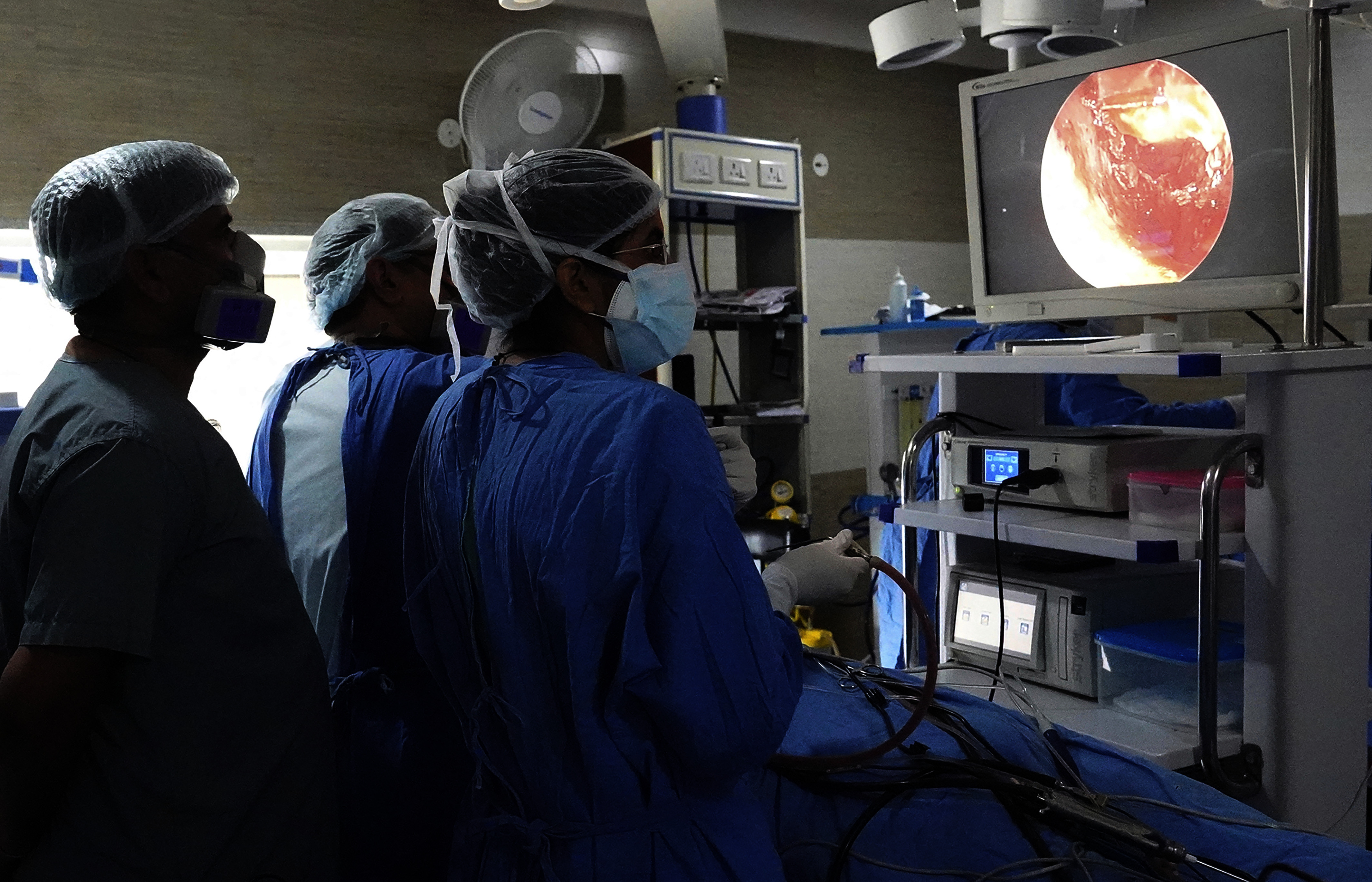 Three members of a medical team in scrubs look at an image on a monitor above the patient.