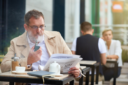 Photograph of a man vaping at an outdoor café with other customers nearby