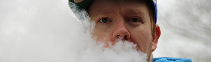 Photograph of a man exhaling a large visible cloud of e-cigarette vapor