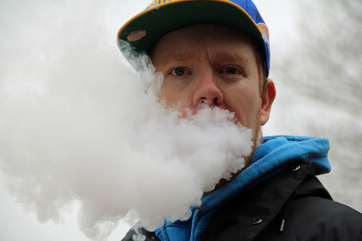 Photograph of a man exhaling a large visible cloud of e-cigarette vapor