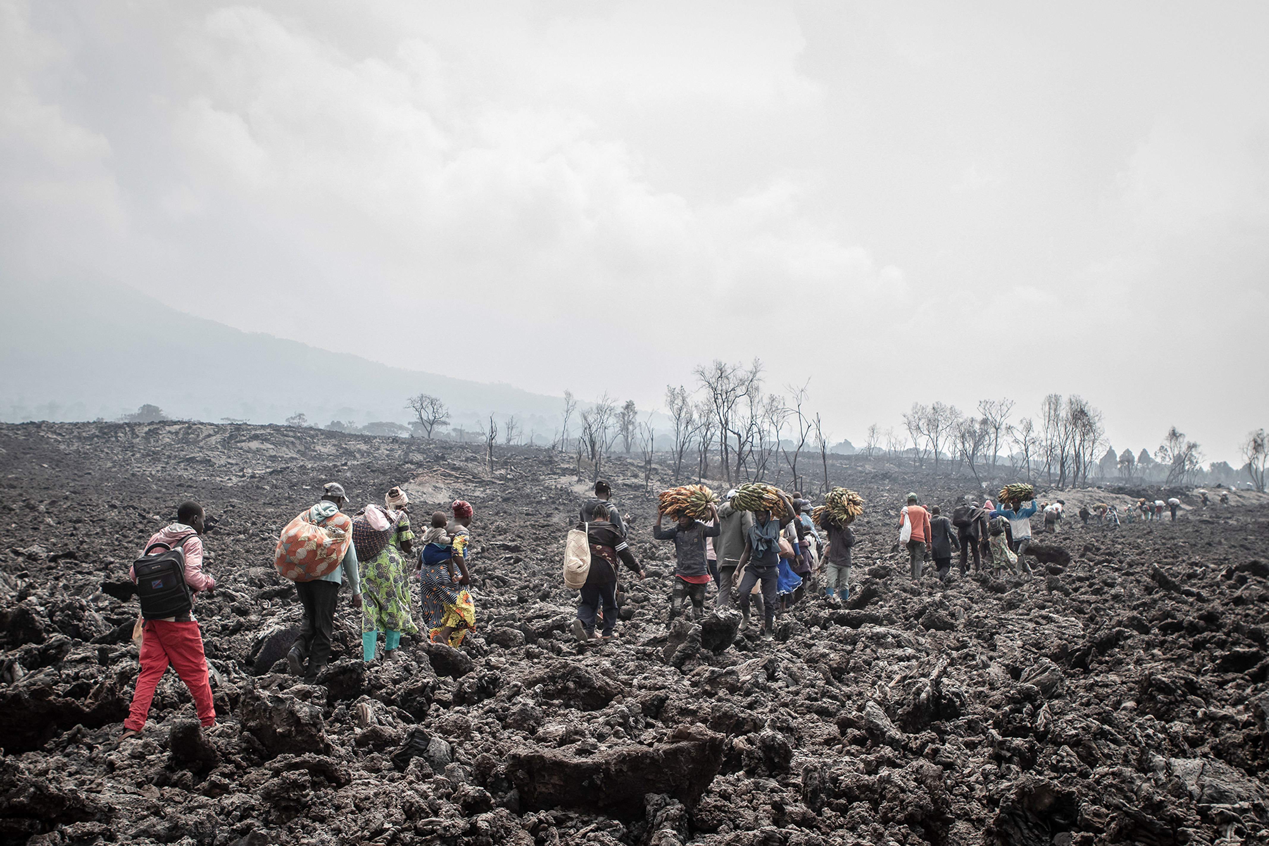 People walking across cooled lava carrying goods and belongings.