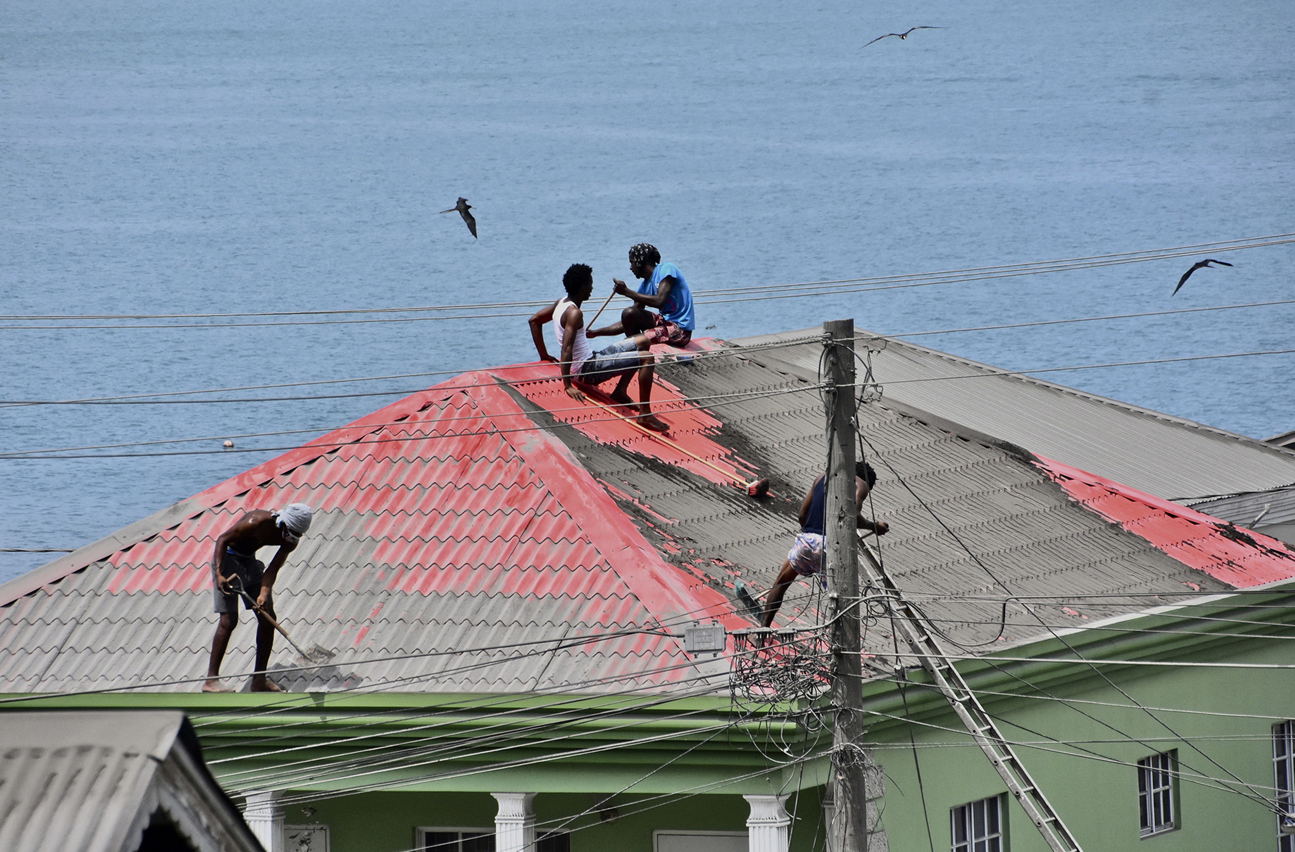 Three men cleaning volcano ash off the roof of a house by the sea.