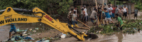 People and machinery clearing debris from flooded canal.