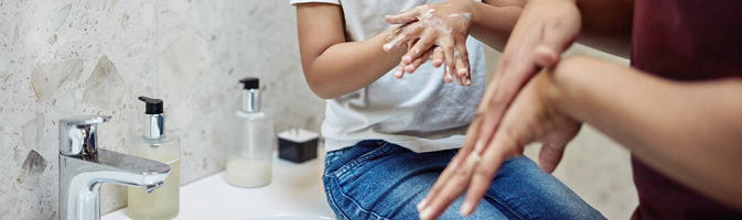 Figure 1: A child sitting on a bathroom sink rubs soap into his hands, as does an adult standing close by.
