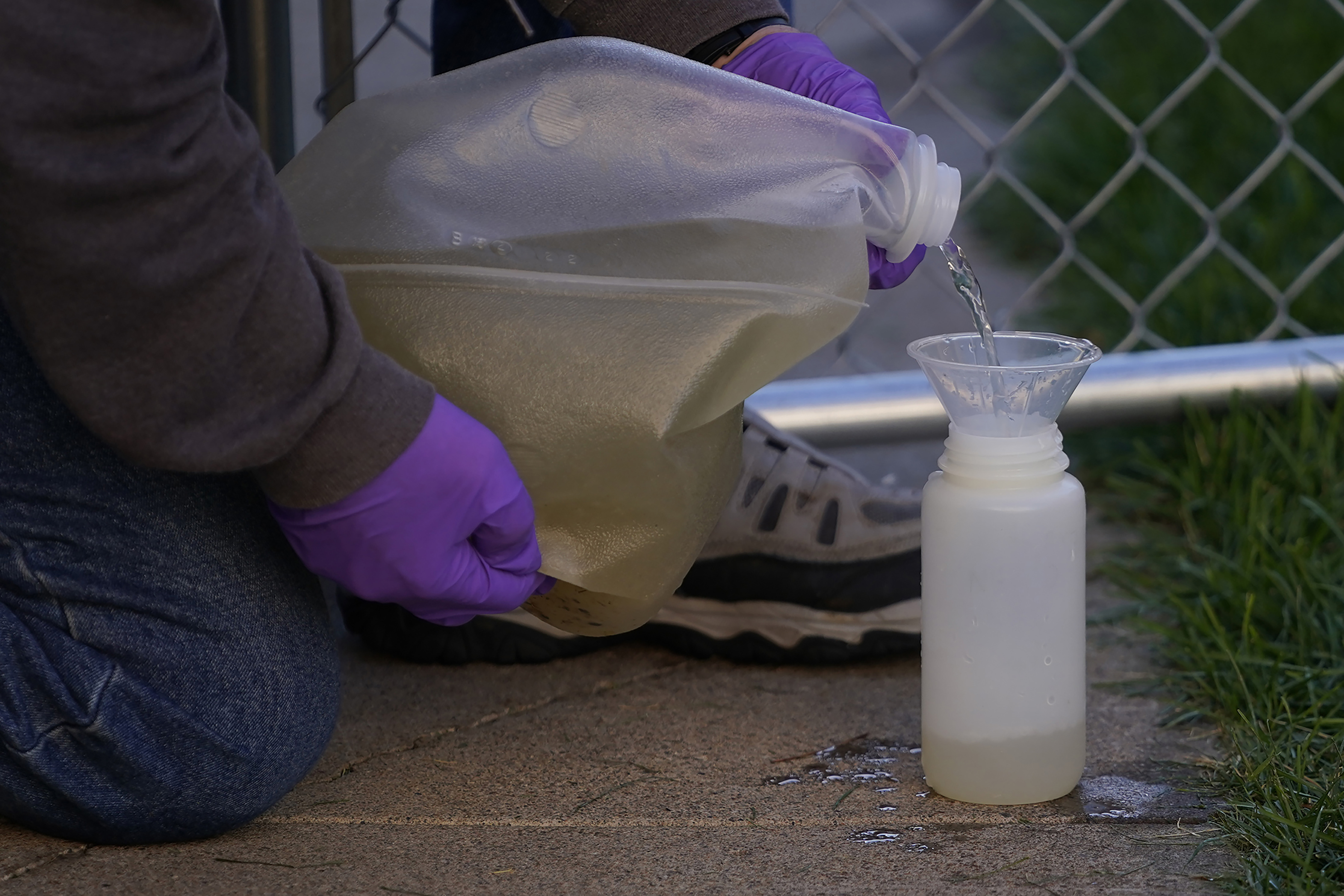 Hands in gloves pouring wastewater into a funnel