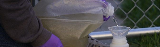 Hands in gloves pouring wastewater into a funnel