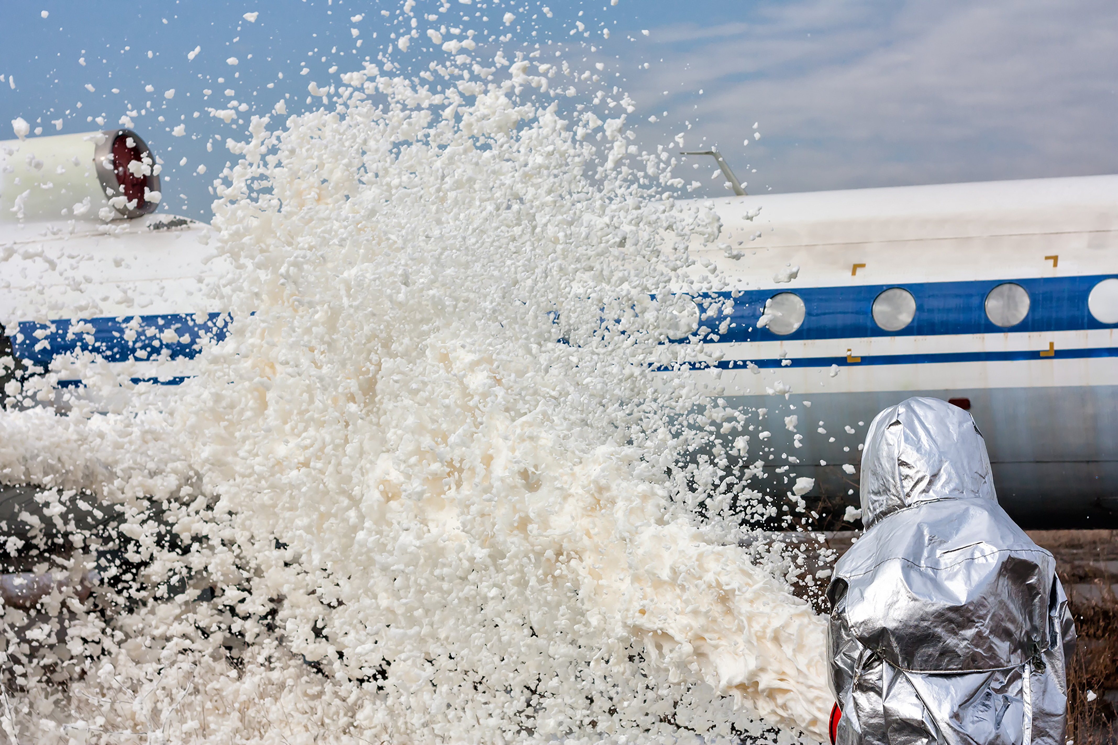 A firefighter spraying foam at a jet