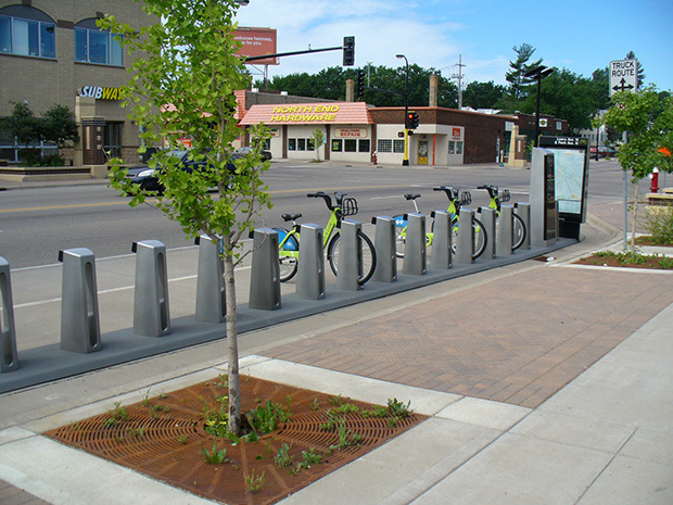 Bike share kiosks, some with bicycles, near a street.