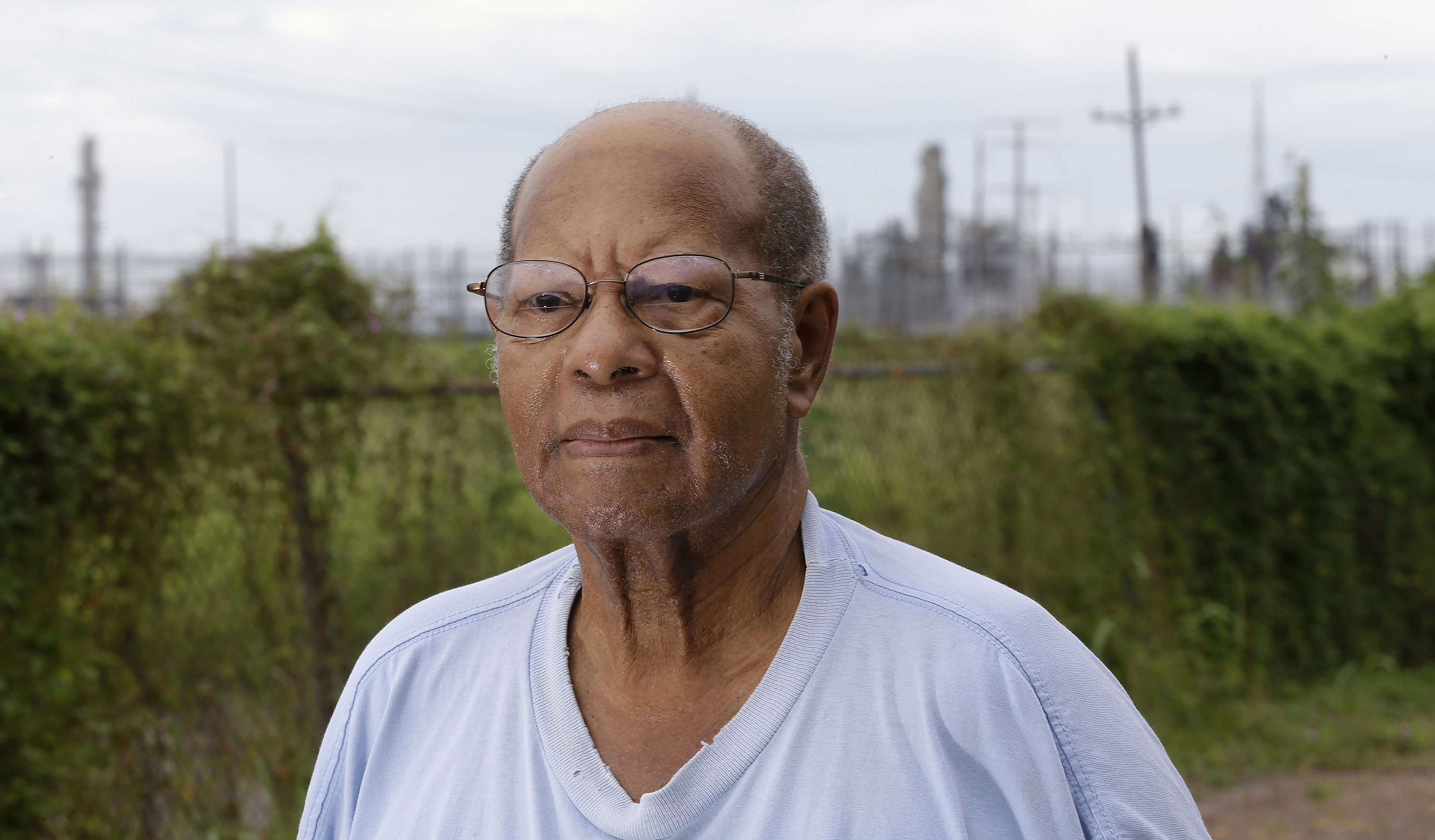 Man in his yard with oil refinery behind him