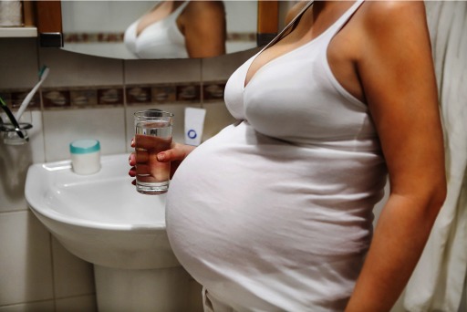 Photograph of a pregnant woman holding a glass of water in her bathroom