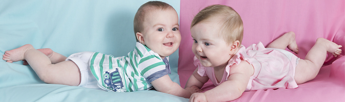 Photograph of an infant boy and an infant girl lying on a blue and pink background