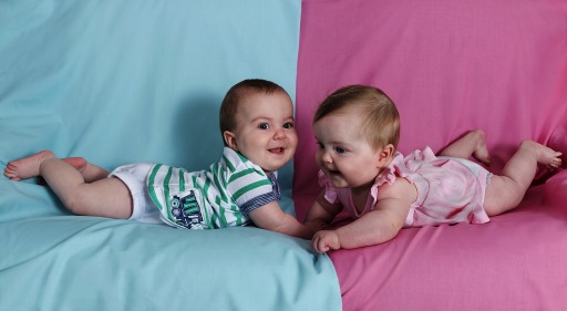 Photograph of an infant boy and an infant girl lying on a blue and pink background