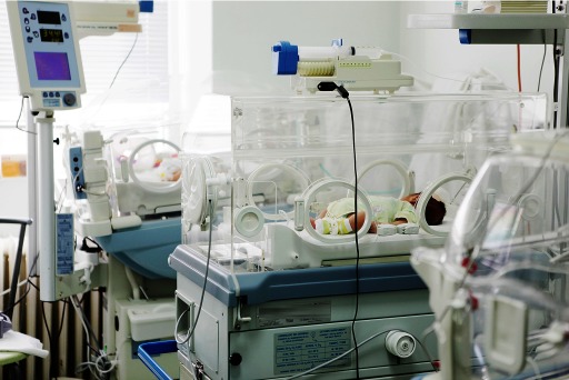 Photograph of a premature baby in an incubator surrounded by bright lights and noisy equipment.