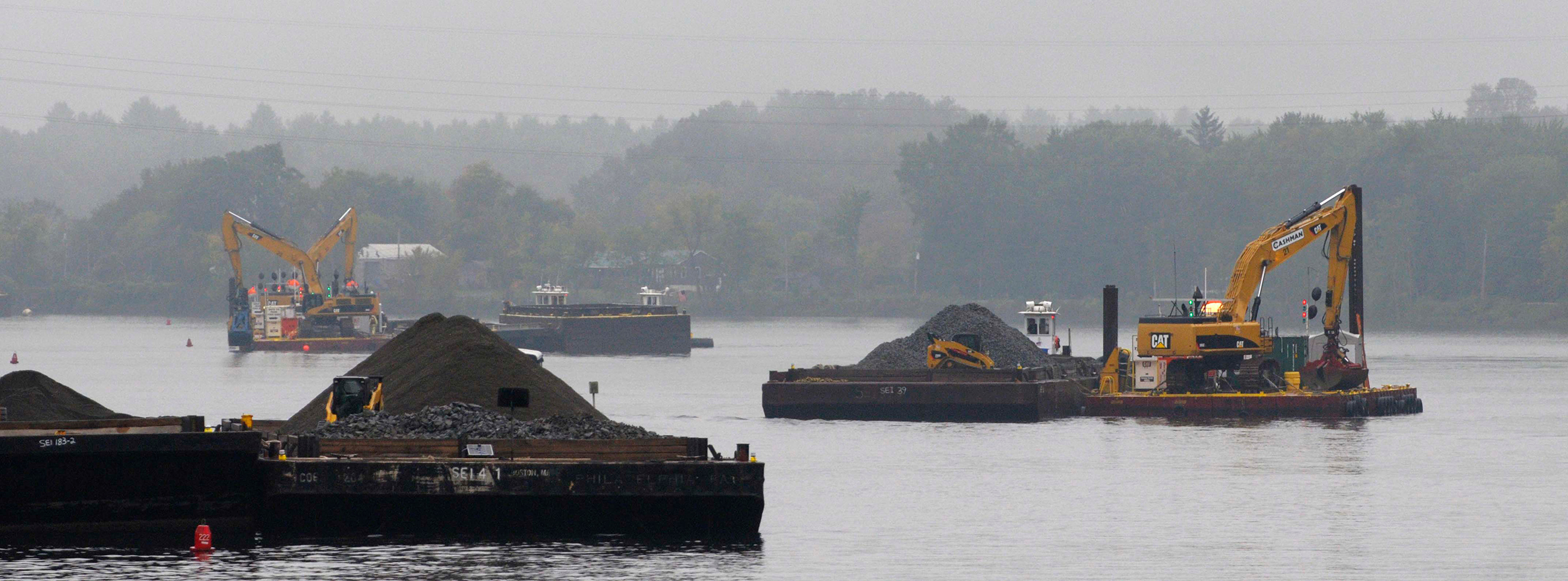 Barges with backhoes and piles of backfill material working on the Hudson River