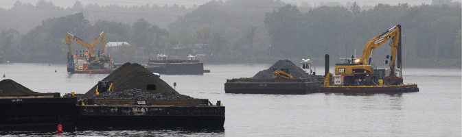 Barges with backhoes and piles of backfill material working on the Hudson River