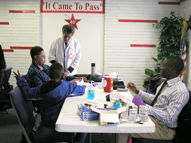 A photograph shows a volunteer nurse providing health information to a Body and Soul program participant at a church kick-off event. Also in the picture is a masters’ degree student who was helping with the event and a participant’s child.