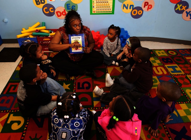 Photograph of a teacher reading to a group of children.