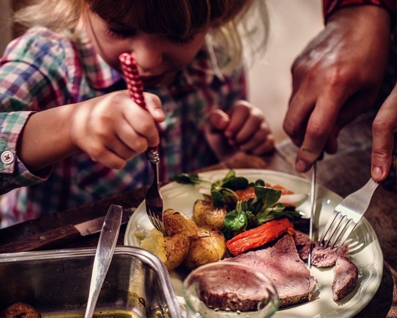 Photograph of a child eating beef and vegetables.