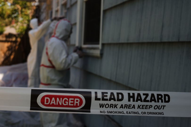 Photograph of workers scraping lead paint from a house exterior.