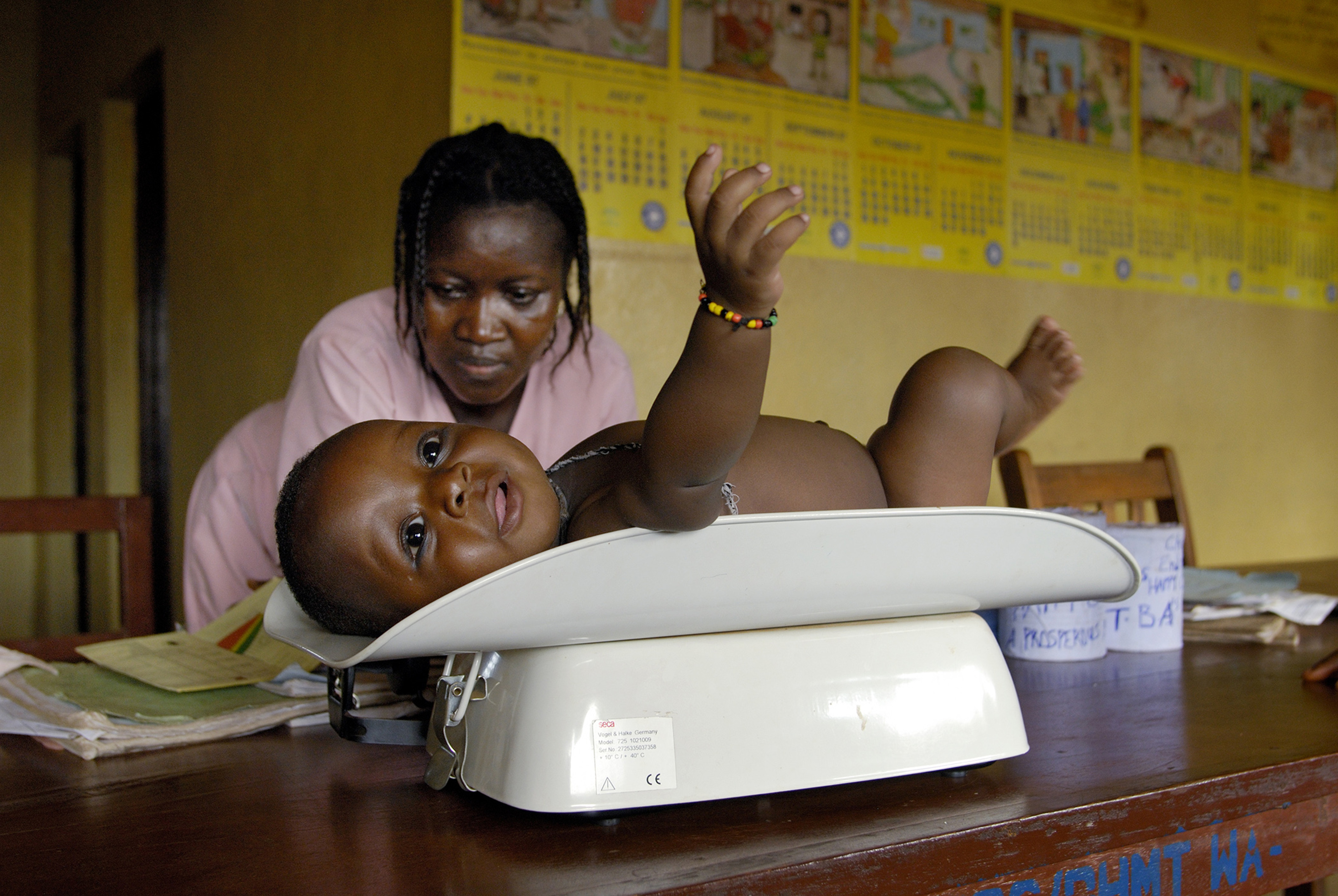 African nurse weighing baby on a scale in a clinic.