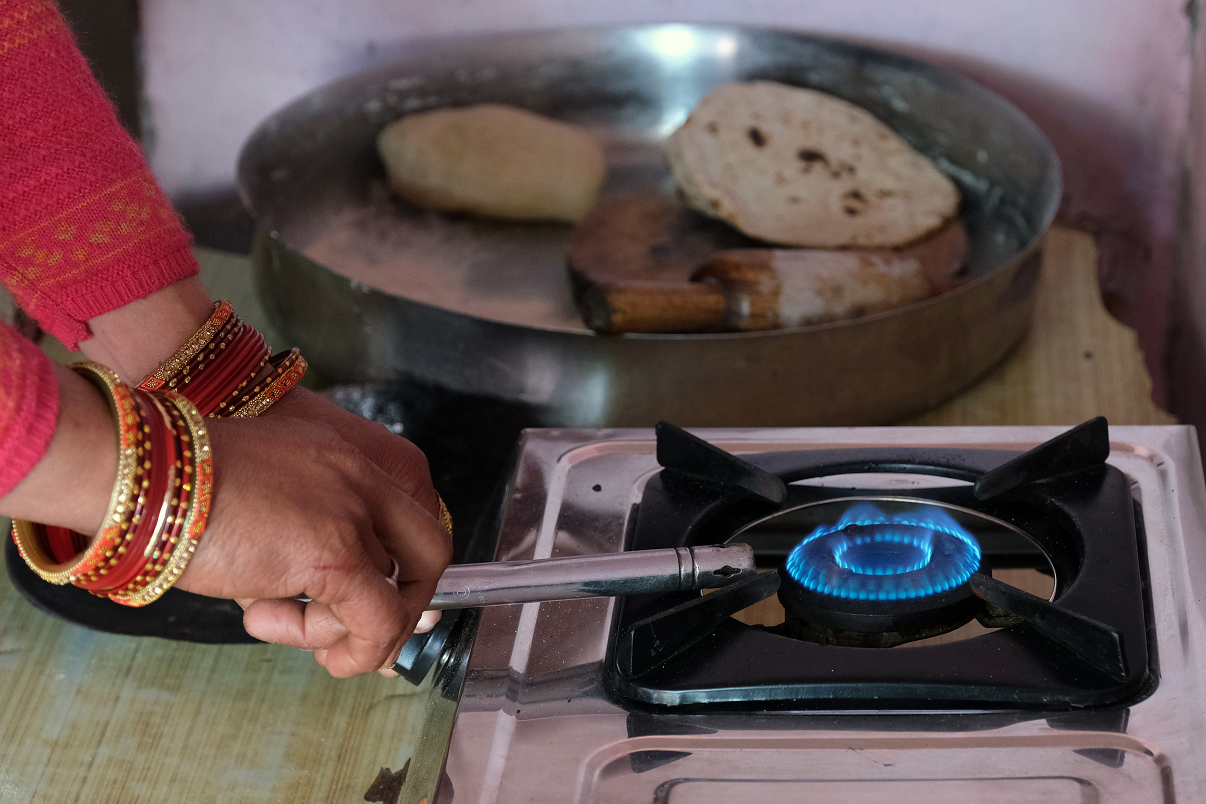 Woman with bangles on wrist lighting a clean gas cooking burner.