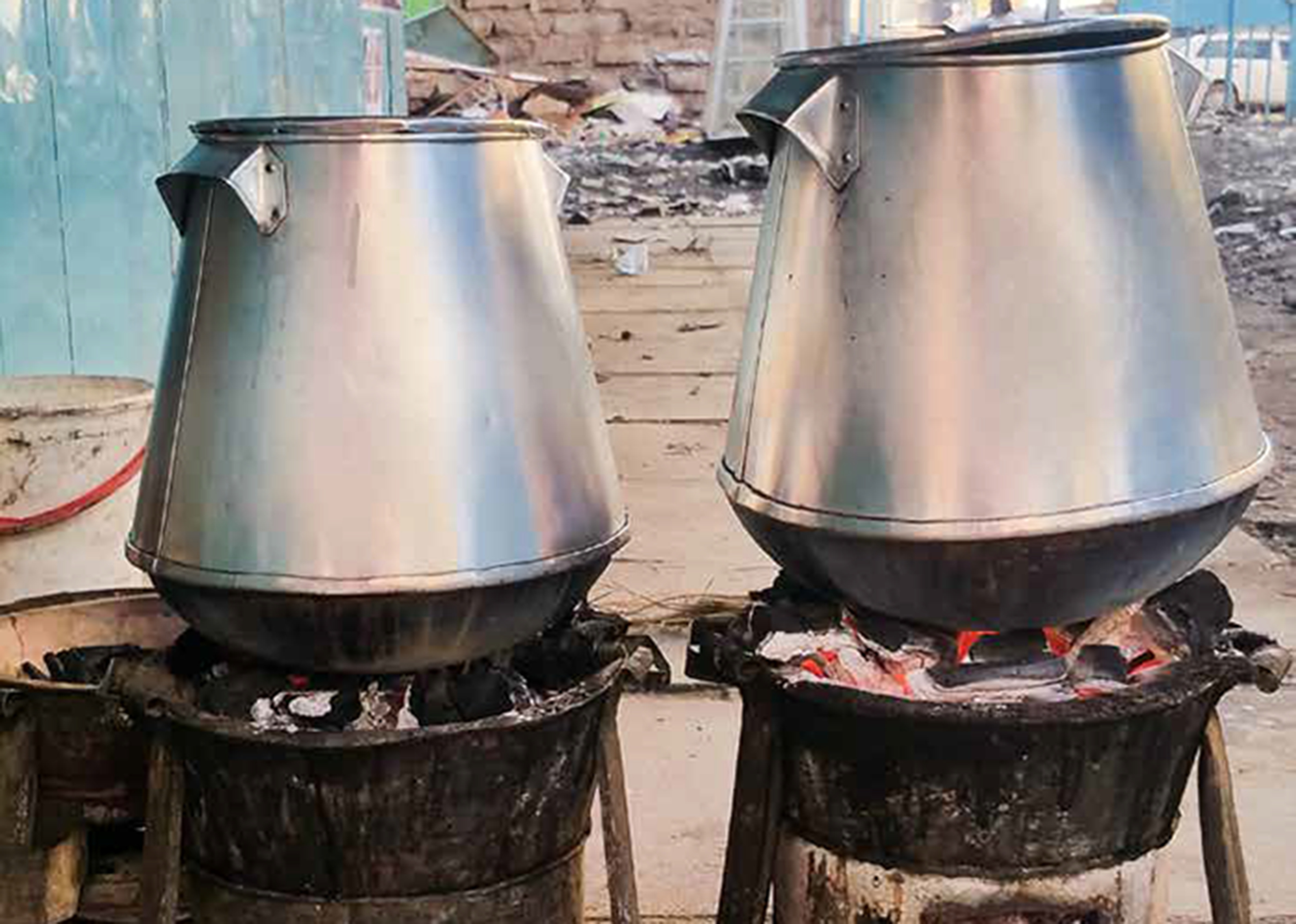 Two large pots on charcoal cookstoves outdoors.